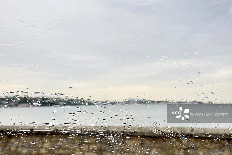 全景拍摄的雨滴在挡风玻璃上，背景是海洋和天空。图片素材