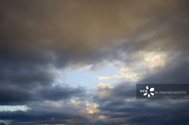 全景拍摄的戏剧性天空，黑暗的云层中有一个蓝色的洞图片素材