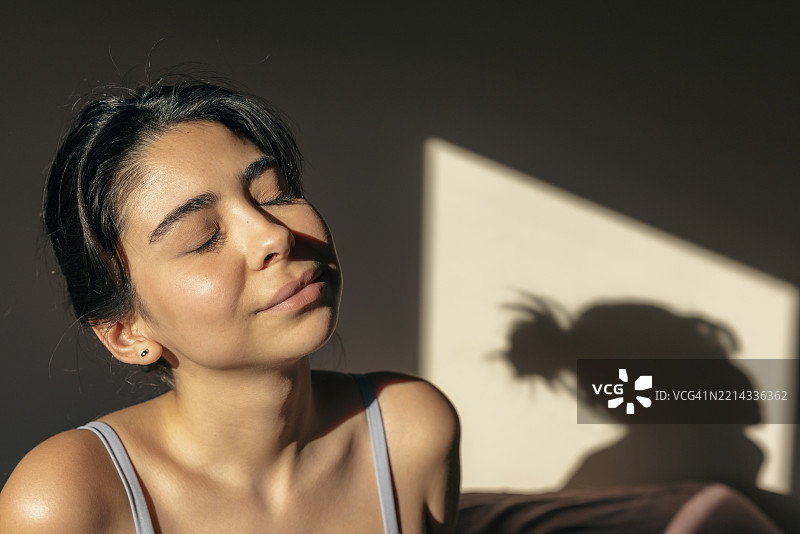 美丽的年轻女性在早晨的床上闭眼练习瑜伽。图片素材