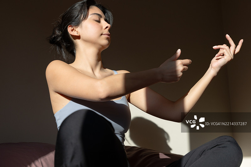 美丽的年轻女性在早晨的床上闭眼练习瑜伽。图片素材