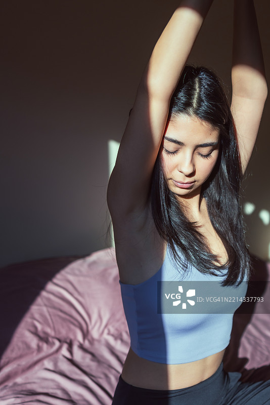 美丽的年轻女性在早晨的床上闭眼练习瑜伽。图片素材