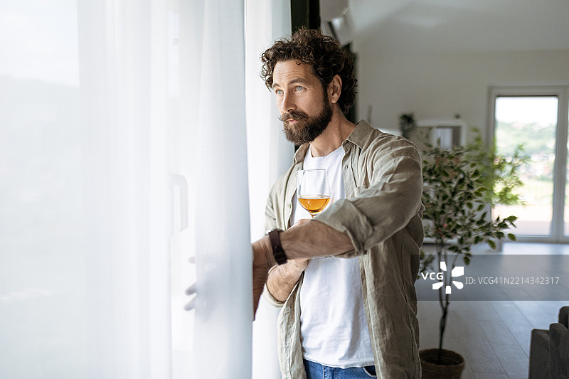 靠在窗边，手握酒杯的沉思年轻男子图片素材