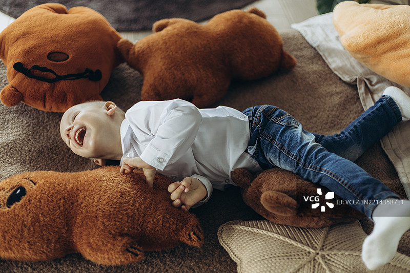 快乐的小男孩躺在床上，周围是大大的毛绒玩具。图片素材