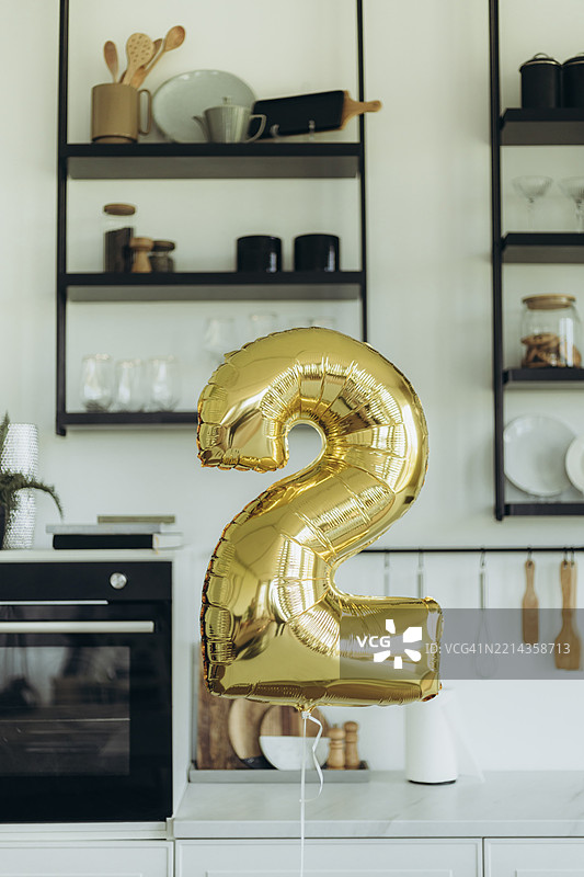 光泽金色的数字2形状铝箔气球漂浮在厨房里。图片素材