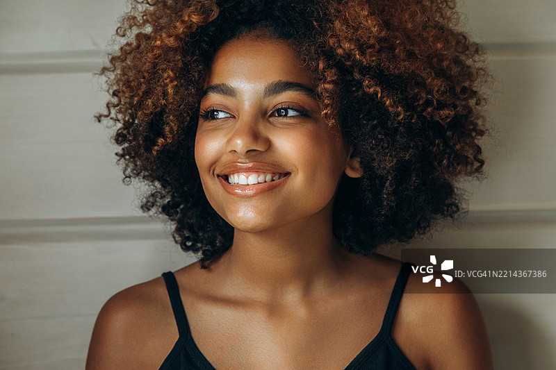 微笑的年轻女性，拥有自然卷曲的头发，身处明亮的室内空间图片素材