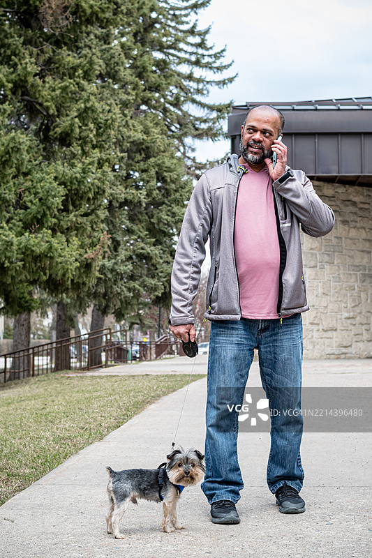 在城市中一名男子一边走狗一边使用手机图片素材