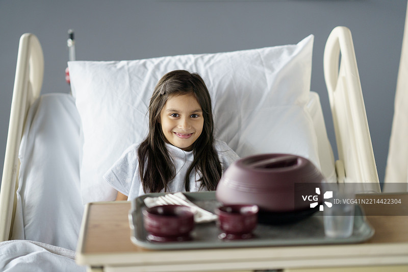 微笑的孩子在医院床上，旁边有静脉输液和医疗设备图片素材