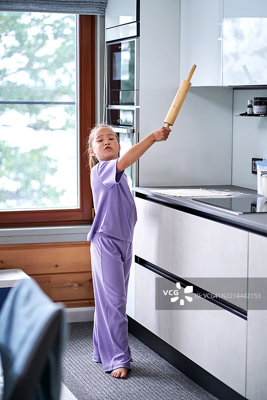 一个9到10岁的女孩穿着紫色的套装，开心地在厨房里擀面团。图片素材