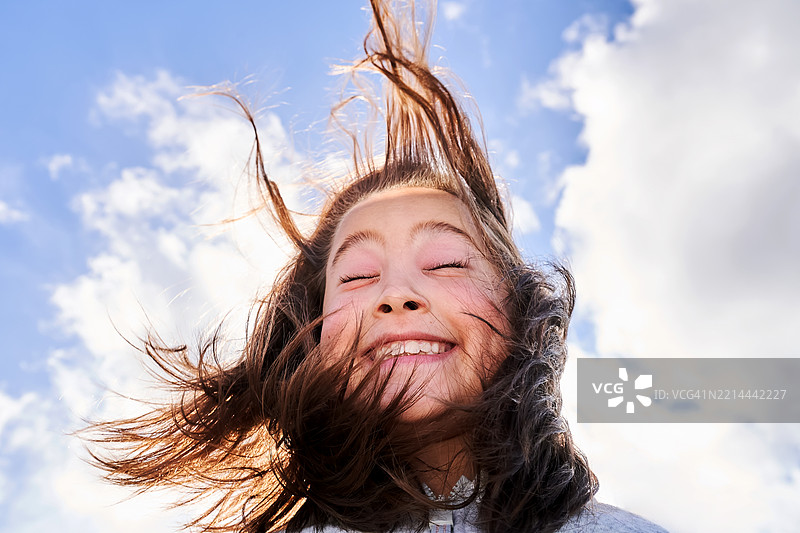 女孩因强风吹乱了她的头发而欢笑，感到非常高兴。图片素材