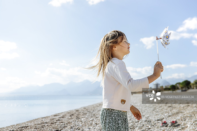 海边的快乐：女孩在沙滩上与风和玩具共舞图片素材