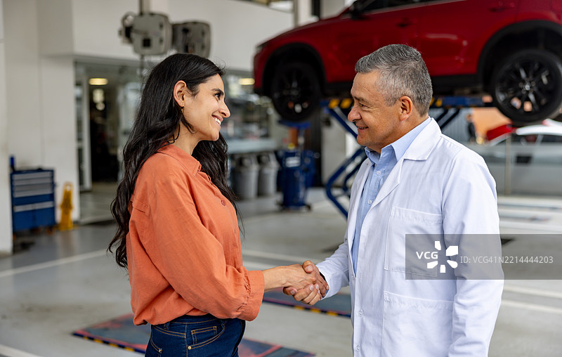女性在汽车修理店与机械师握手，准备将她的车留在那里。图片素材