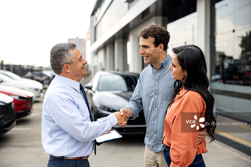 汽车经销商的销售员与一对夫妇握手问候图片素材