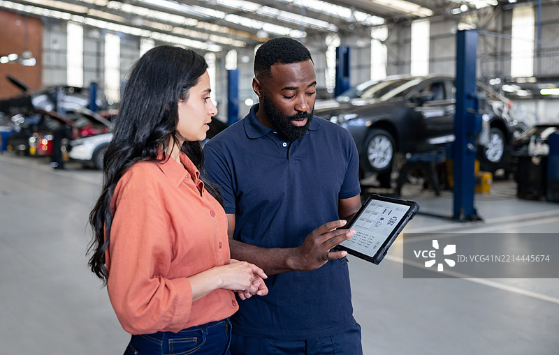 机械师正在用平板电脑向一位女性展示她汽车的诊断结果图片素材