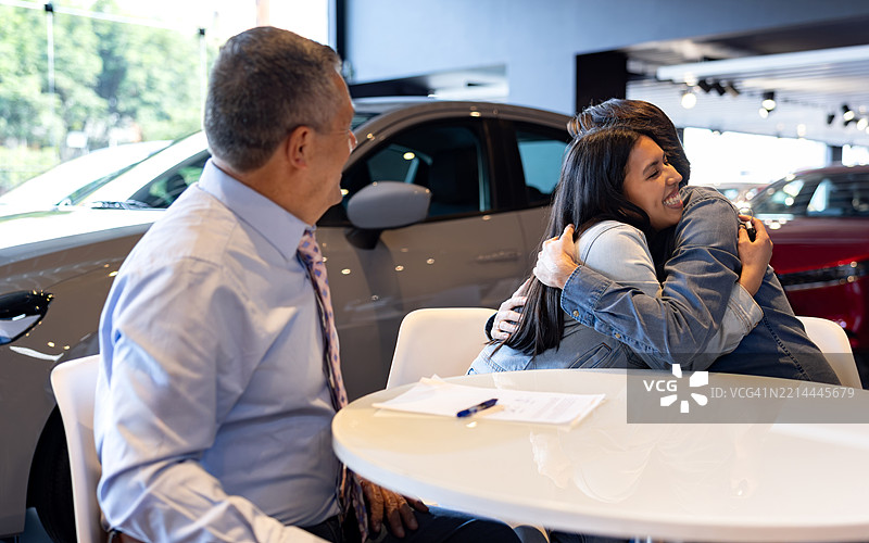 父亲和女儿在汽车经销商处买车后拥抱在一起图片素材