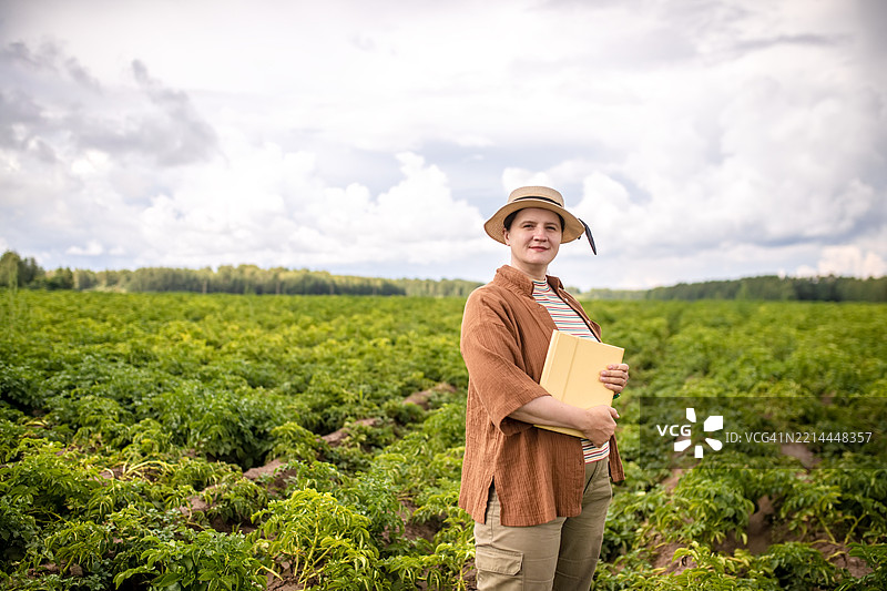 戴着帽子的胖型女性农民在土豆田里手持平板电脑。图片素材