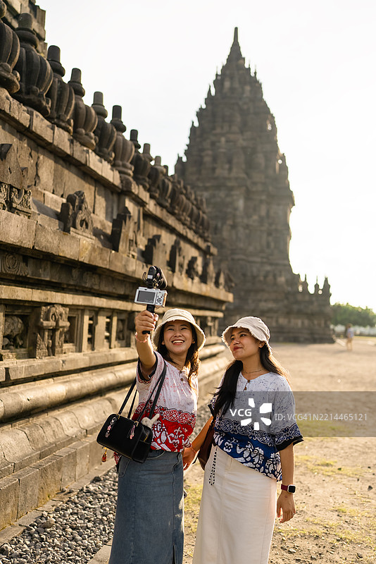 女性友谊影响者佩戴牛仔帽，使用摄像机和麦克风在旅行中讲解普兰巴南寺。图片素材