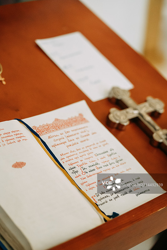 在宗教仪式中，木桌上放着一本打开的书、一枚银色十字架和一张纸。图片素材