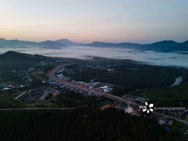 宁静的乡村小镇鸟瞰图，坐落在山谷中，低洼的雾气和柔和的黎明光线映照在地平线上。图片素材