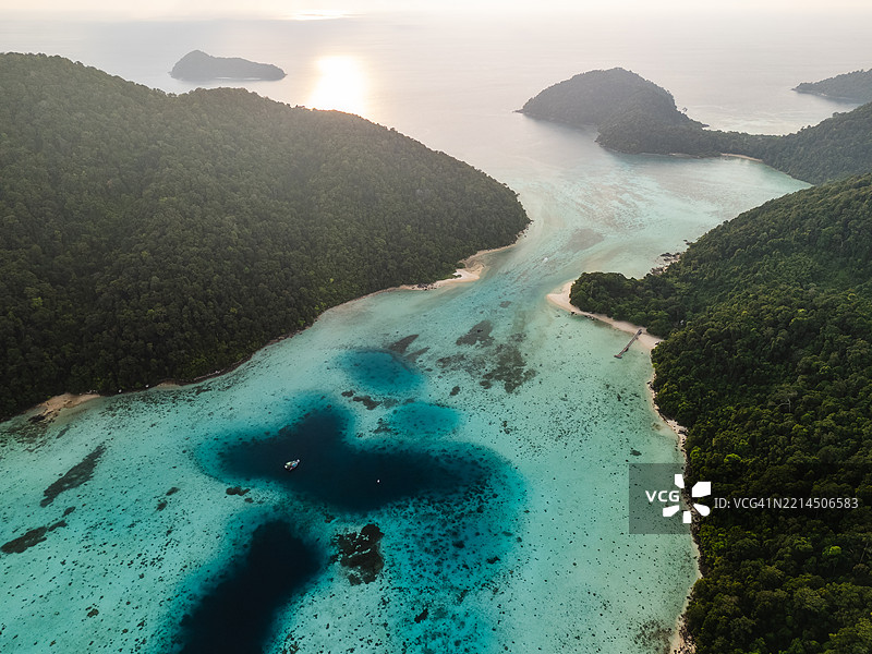 日落时分，丛林覆盖的岛屿的鸟瞰图，碧绿色的浅滩、深蓝色的泻湖、珊瑚礁和宁静的海岸线。图片素材