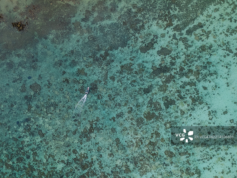 热带海域上空俯瞰一只船在清澈的绿松石色水面上航行，水下是浅海珊瑚礁。图片素材