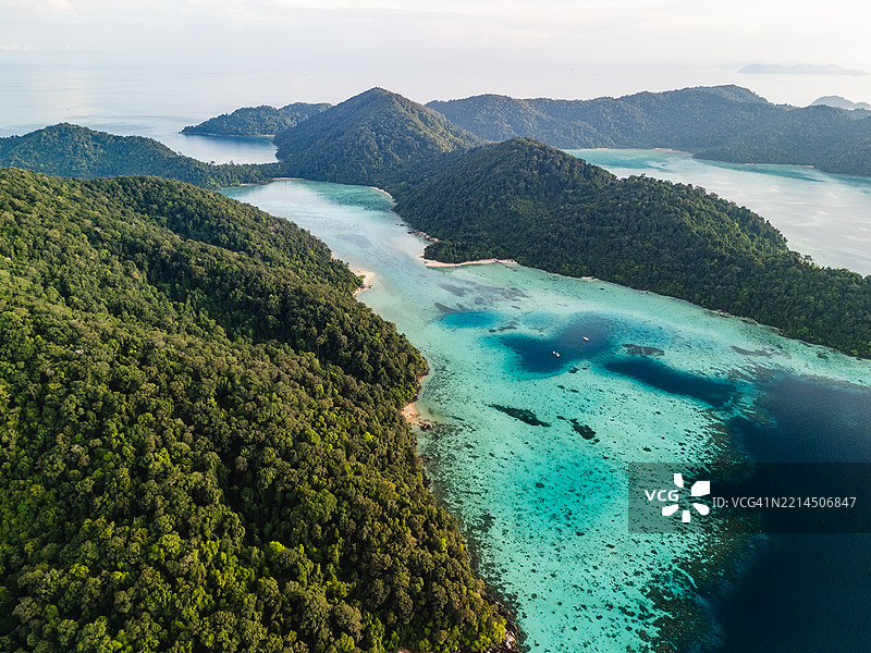 密集绿色热带岛屿的鸟瞰图，四周环绕着碧蓝的泻湖水域和珊瑚礁，非常适合生态旅游和探险。图片素材