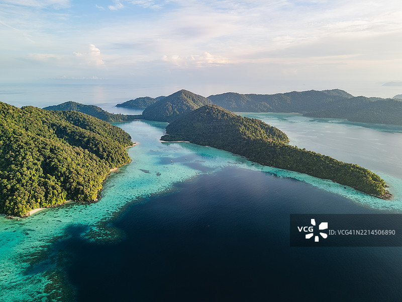 多个郁郁葱葱的热带岛屿的鸟瞰图，四周环绕着清澈的碧绿色海水和珊瑚礁，天空部分多云。图片素材