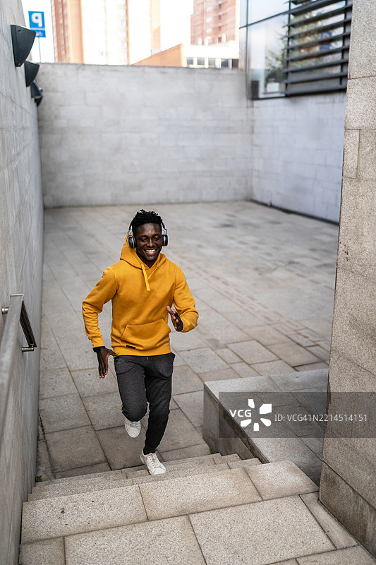 年轻的黑人男子戴着耳机跑上楼梯听音乐图片素材