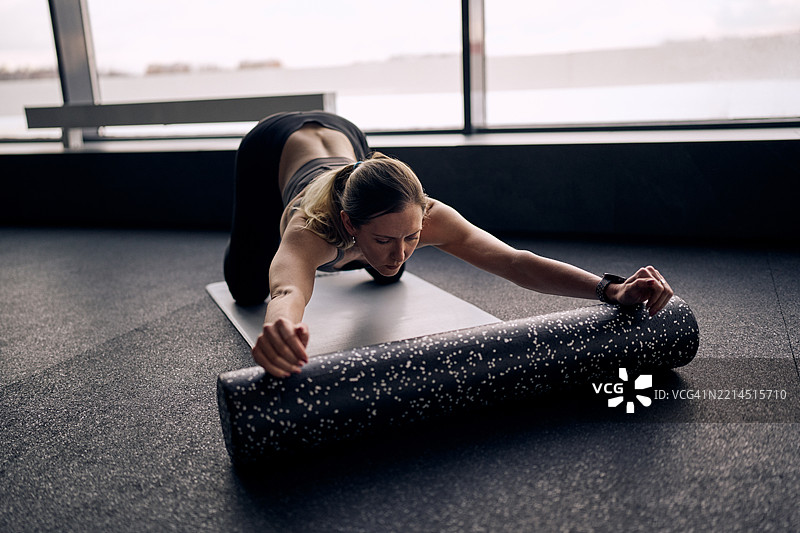 专注的女性在瑜伽垫上使用泡沫轴拉伸图片素材