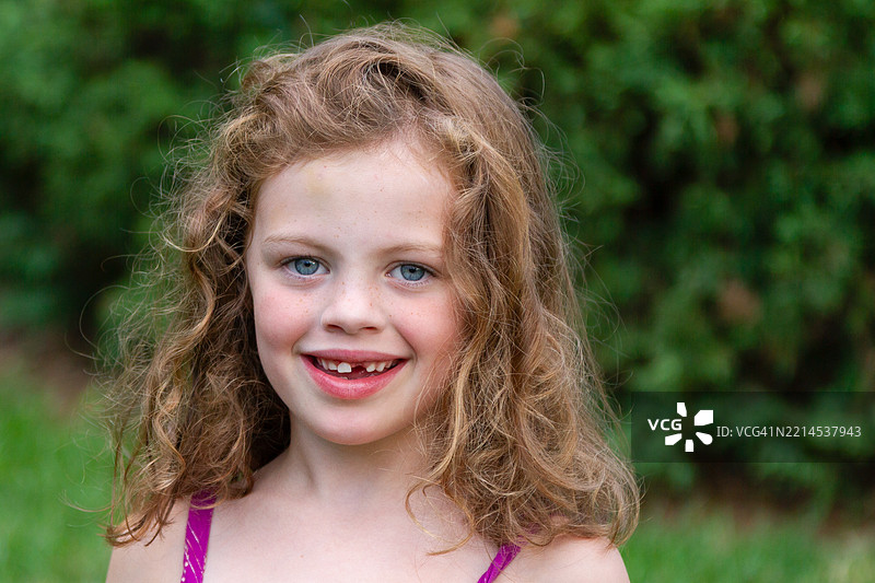 可爱的小女孩在夏天的傍晚微笑着看向镜头，缺了一颗门牙。图片素材