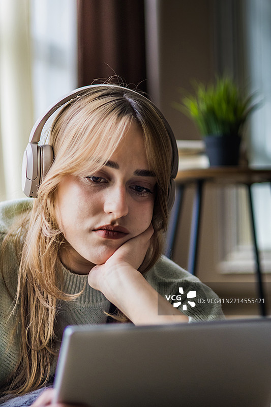 美丽的年轻女性戴着耳机，在家中使用数字平板电脑进行投资。在线购物、电子学习、社交网络或在线工作是Z世代日常生活的一部分。图片素材