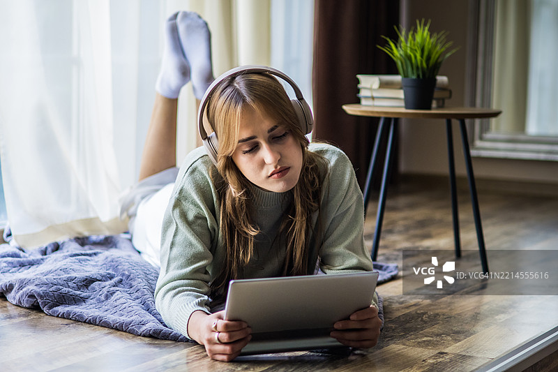 美丽的年轻女性戴着耳机，在家中使用数字平板电脑进行投资。在线购物、电子学习、社交网络或在线工作是Z世代日常生活的一部分。图片素材