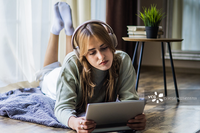 美丽的年轻女性戴着耳机，在家中使用数字平板电脑进行投资。在线购物、电子学习、社交网络或在线工作是Z世代日常生活的一部分。图片素材