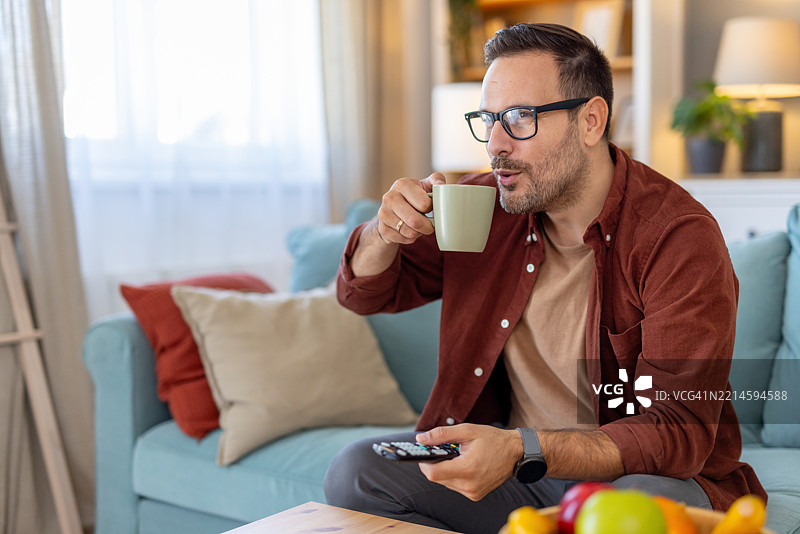 男人在客厅里喝咖啡，享受电视节目图片素材