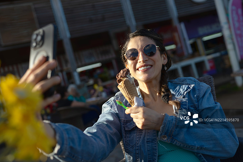 快乐的孕妇游客在户外吃冰淇淋时自拍图片素材