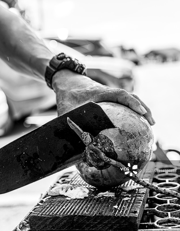 男子在库拉索的街头摊位熟练地用砍刀劈开新鲜椰子。图片素材