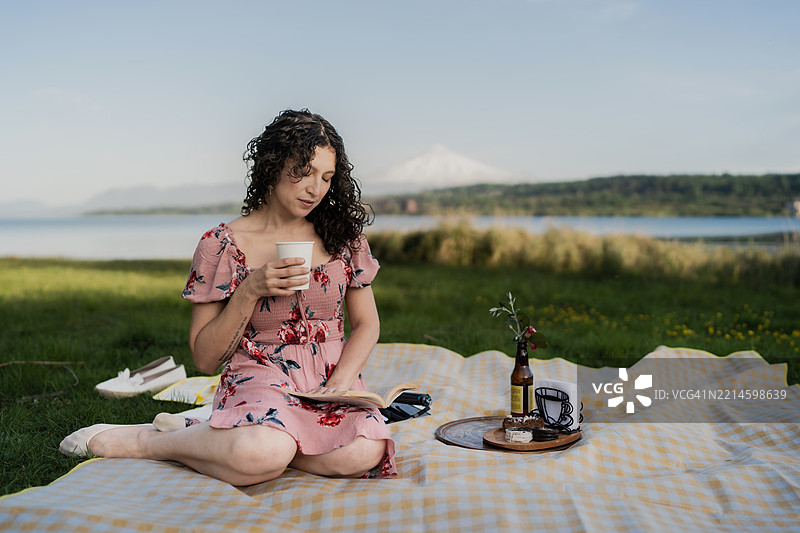 女人在湖边享受轻松的野餐，手里拿着一本书和咖啡图片素材