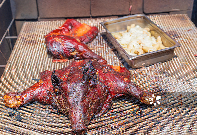 整只烤猪和传统配菜在箱式烤架中烹饪。图片素材