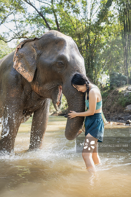 年轻的泰国女性在河中拥抱大象图片素材