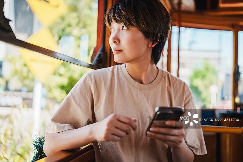 年轻的亚洲女性一边看着电车窗外，一边拿着手机。图片素材