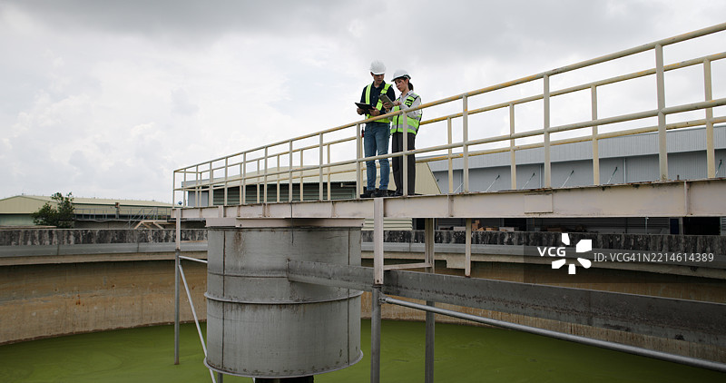 从空中俯瞰两位环境工程师在污水处理厂工作，愉快地合作开发创新的水管理解决方案。图片素材