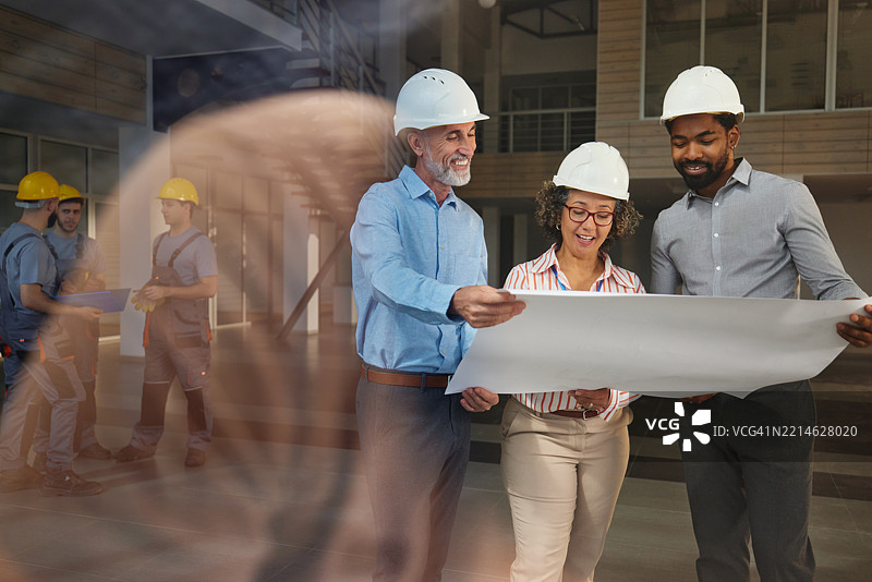 快乐的室内设计师在建筑工地上阅读设计图纸。图片素材