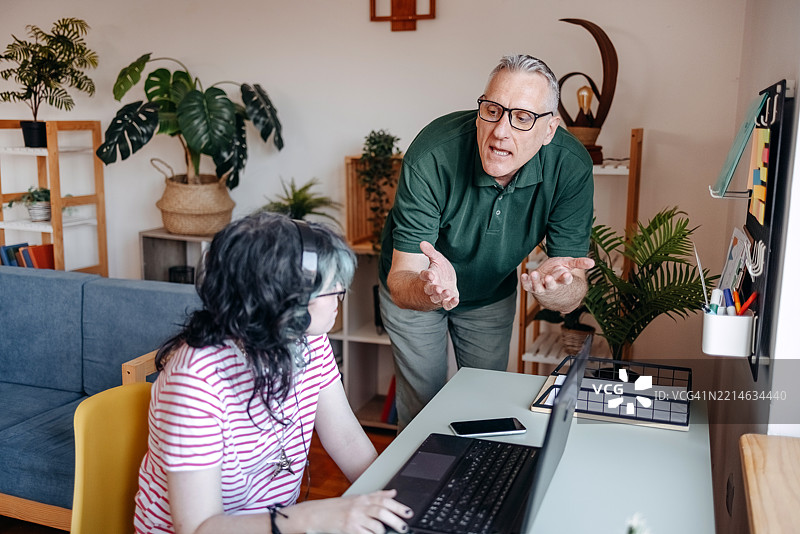 父亲在家中与他的 teenage 女儿进行严肃的谈话，她坐在笔记本电脑前。图片素材
