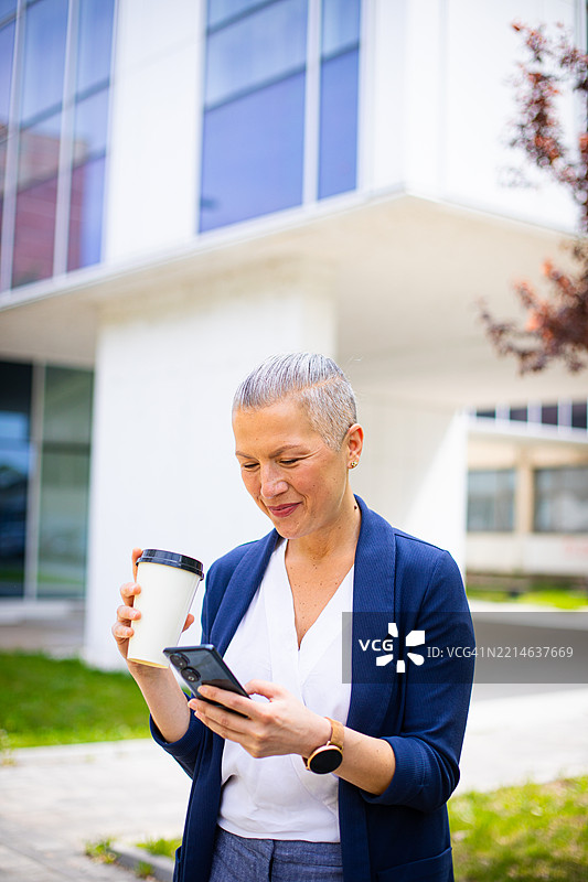 在现代办公大楼前使用手机的女商人图片素材