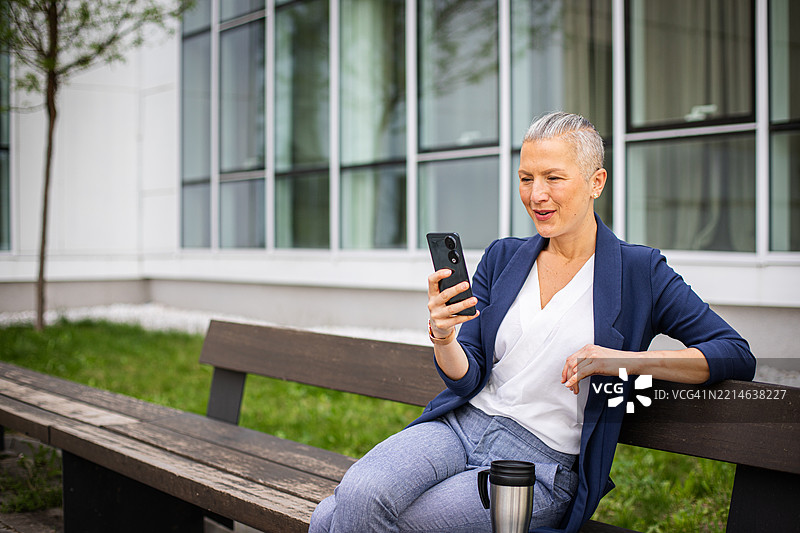 坐在长椅上休息的女商人，正在用手机。图片素材
