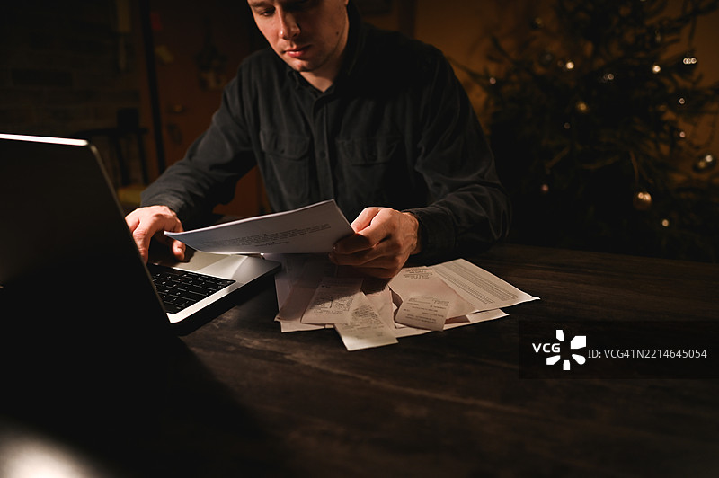 在圣诞假期，压力大的男人在家用笔记本电脑计算家庭账单图片素材