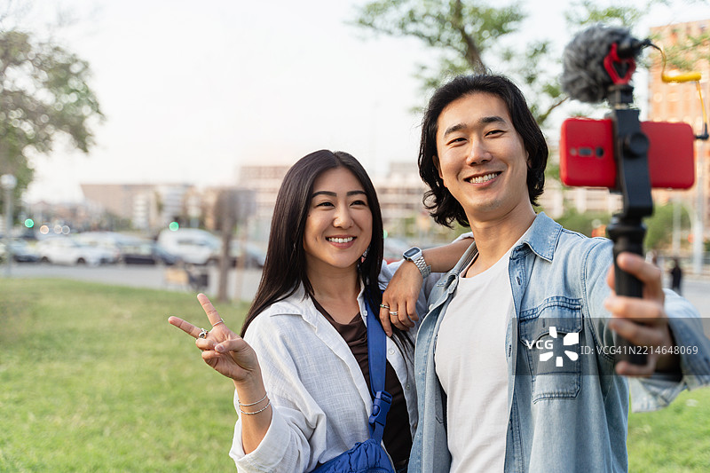 年轻的亚洲情侣年轻网红在公园使用手机稳定器和麦克风拍摄视频博客内容图片素材
