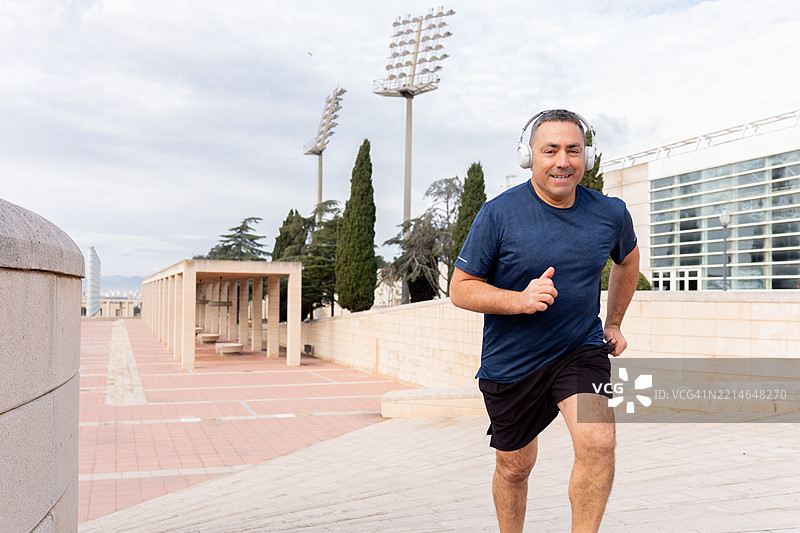 适合中年男性在城市街道上跑步，佩戴无线耳机听音乐，体现积极健康的生活方式图片素材