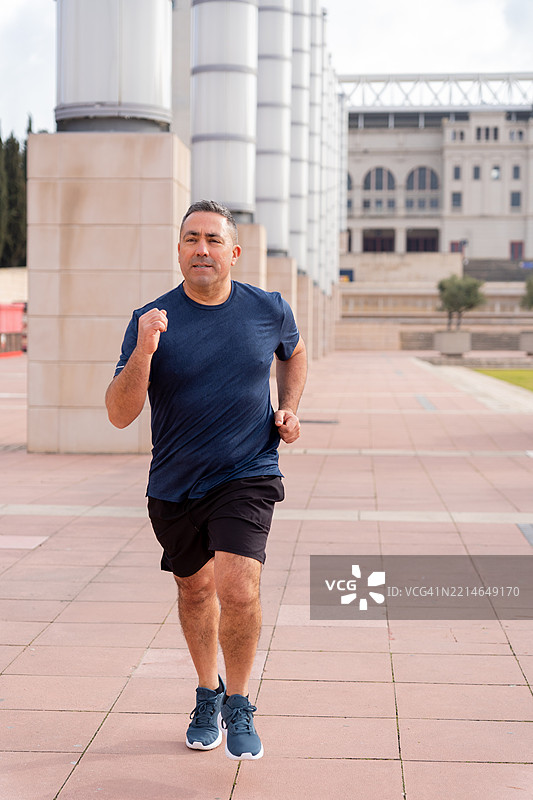 中年男子在城市景观中慢跑，穿着时尚运动服，拥抱健康积极的生活方式图片素材