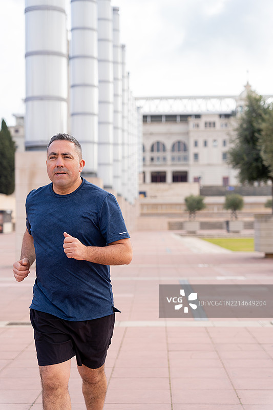 中年男子在巴塞罗那的城市街道上慢跑，穿着时尚的运动服，享受积极健康的生活方式。图片素材