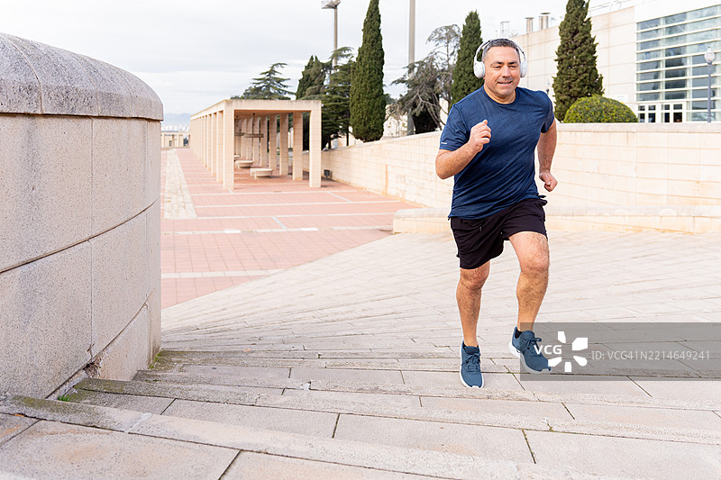 中年男子在城市公园里一边跑上楼梯一边戴着耳机听音乐图片素材